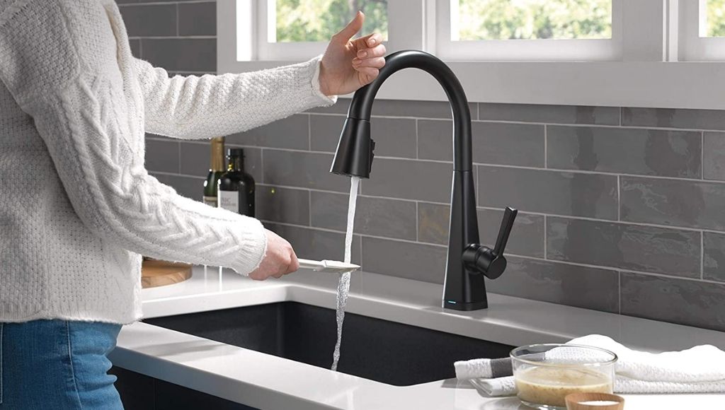 A woman cleans a spoon at a touchless pool-down kitchen faucet